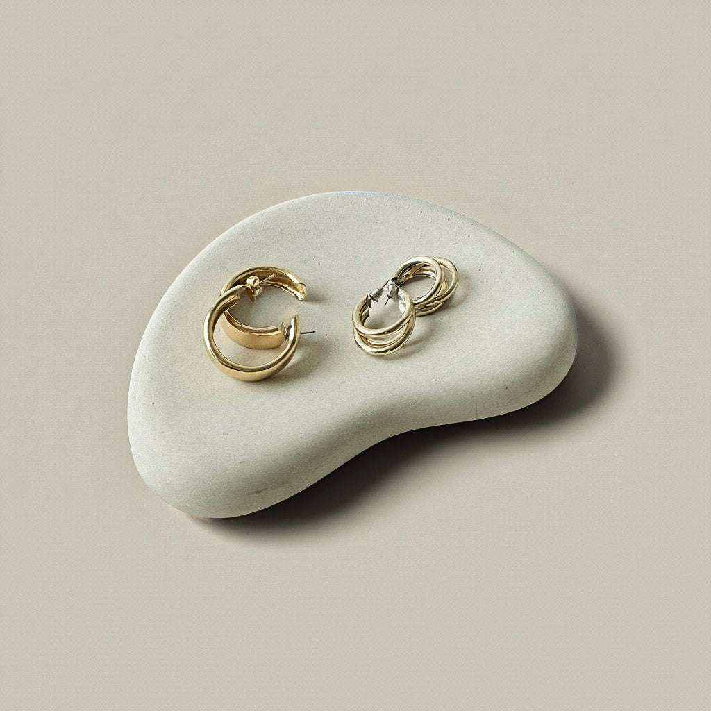 minimalistinis betono padėklas Yin su aukso spalvos auskarais ant neutralaus fono