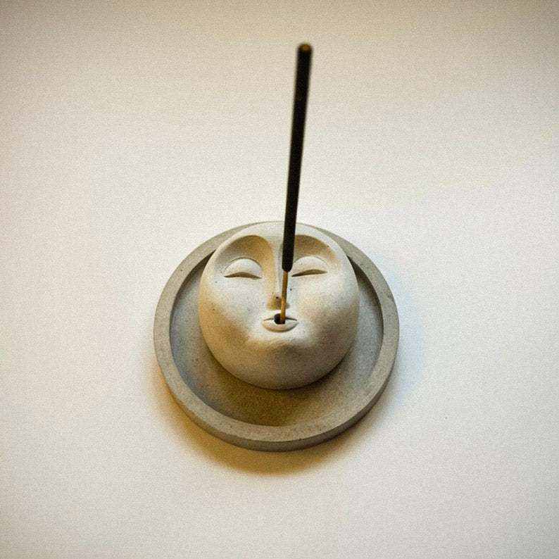 minimalistinė betono smilkalinė ir padėkliukas su veido motyvu meditacijai ir namų harmonijai