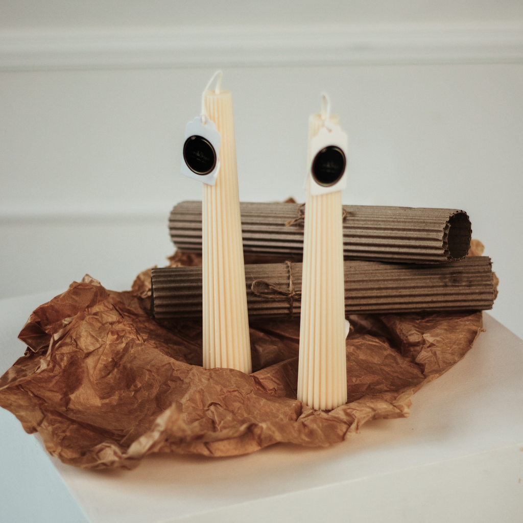 Sojų vaško žvakė "Mila" su minimalistinėmis linijomis ir trapecijos forma ant rudos pakavimo medžiagos.