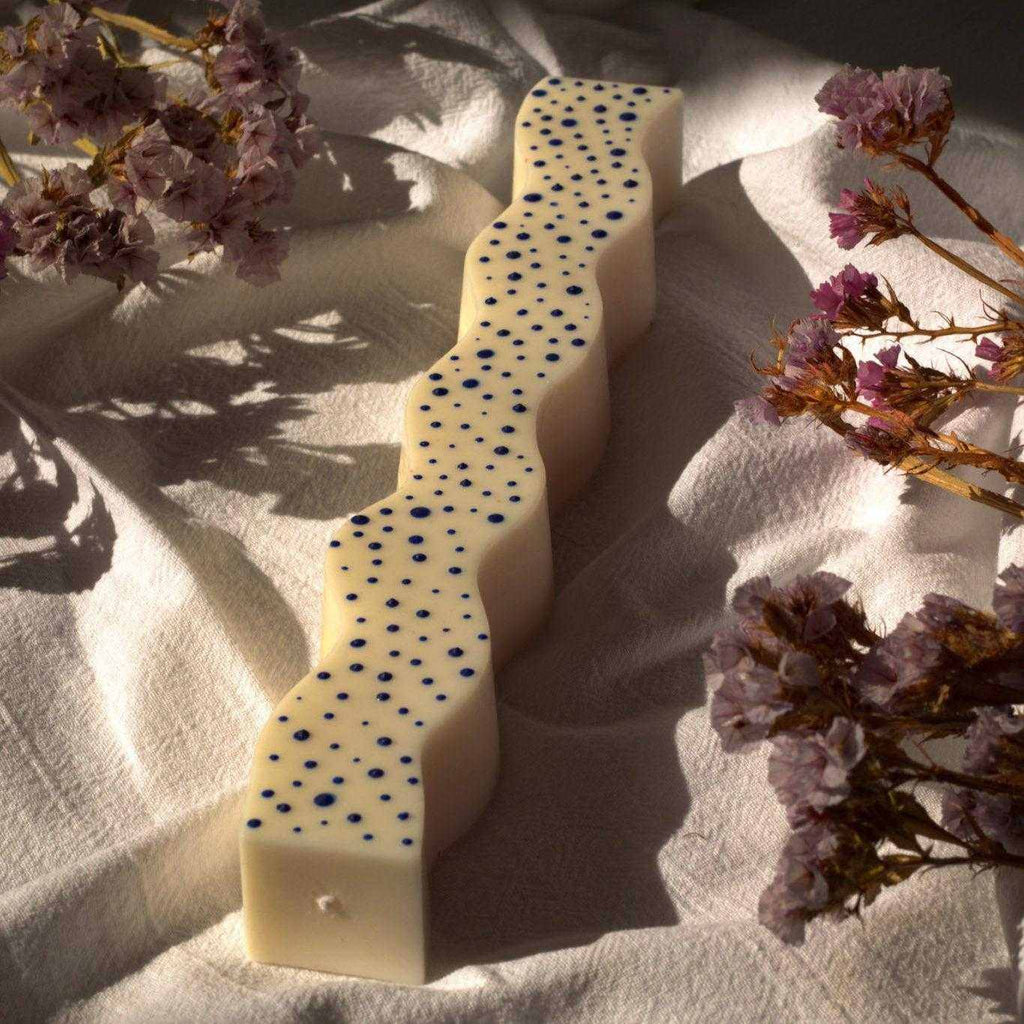 Dekoruota sojų vaško žvakė su mėlynais tašeliais ir bangelėmis ant natūralaus fono