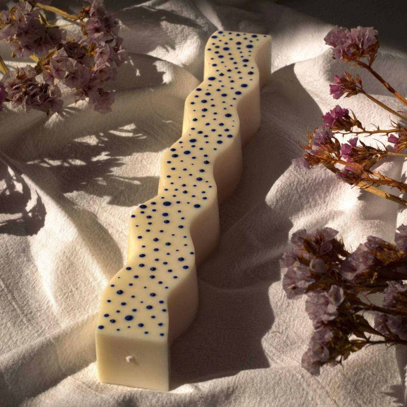 Dekoruota sojų vaško žvakė su mėlynais tašeliais ir bangelėmis ant natūralaus fono