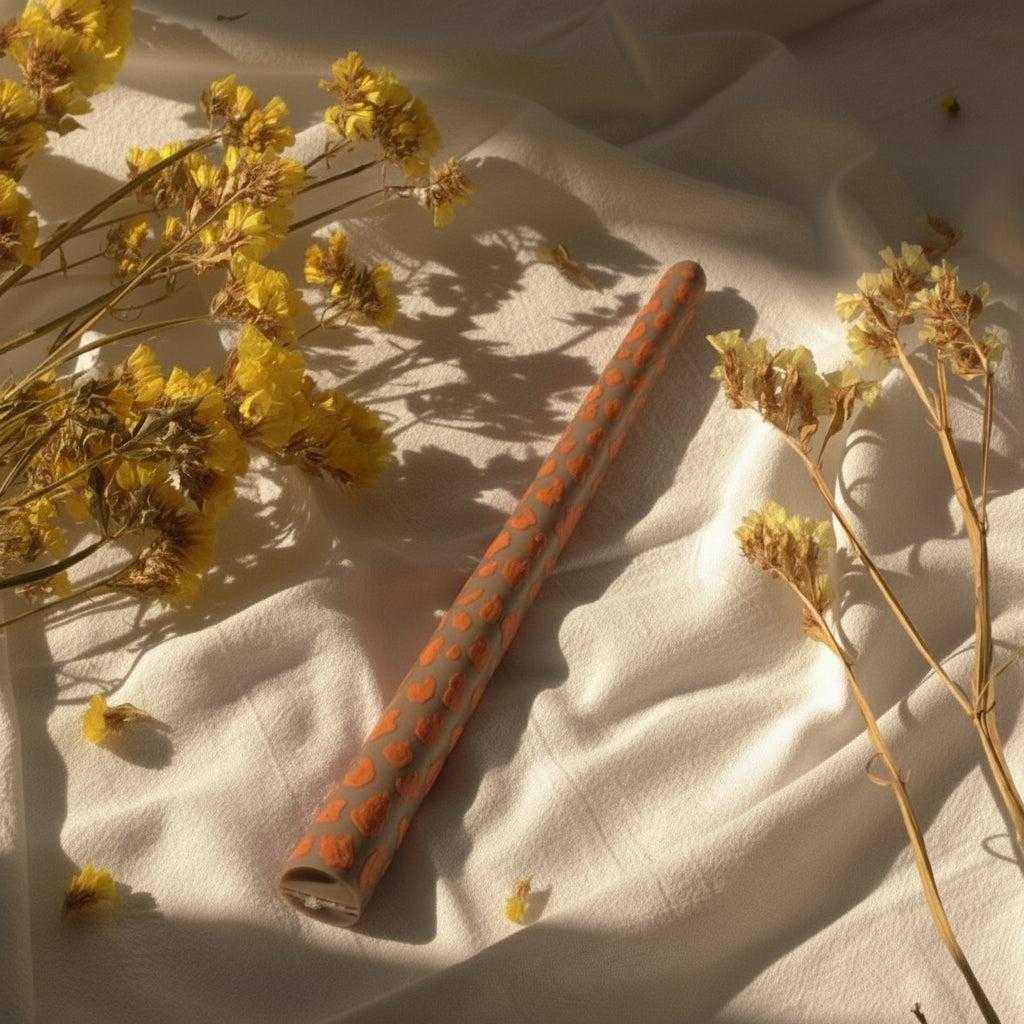 Dekoruota plona sojų vaško žvakė su rankų darbo raštais ant šviesaus fono su džiovintais geltonais žiedais