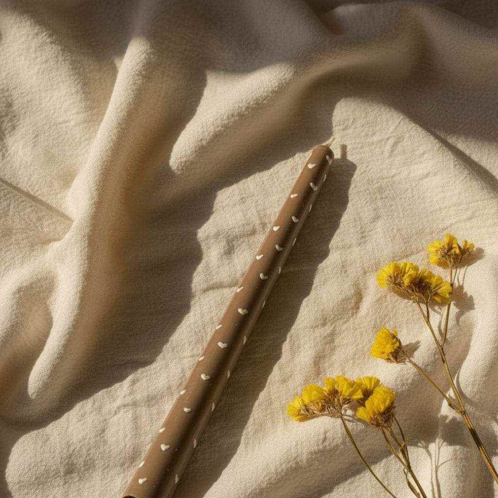 Dekoruota sojų vaško žvakė „Slim Glow“ ant natūralaus audinio šviesos fone su geltonais džiovintais augalais