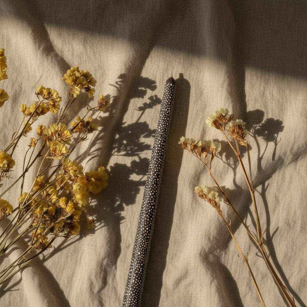 Dekoruota plona sojų vaško žvakė su rankų darbo ornamentais ant smėlio spalvos fono su džiovintais žiedais