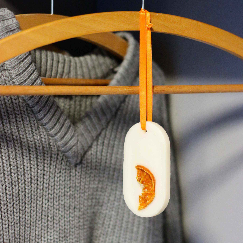 natūralus spintos kvapukų rinkinys su džiovinto citruso gabalėliu ir oranžine juostele ant kabykla kabančio megztinio fone