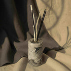 Betoninis difuzorius su aromatinėmis lazdelėmis ir marmurinio rašto dizainu ant audinių fono