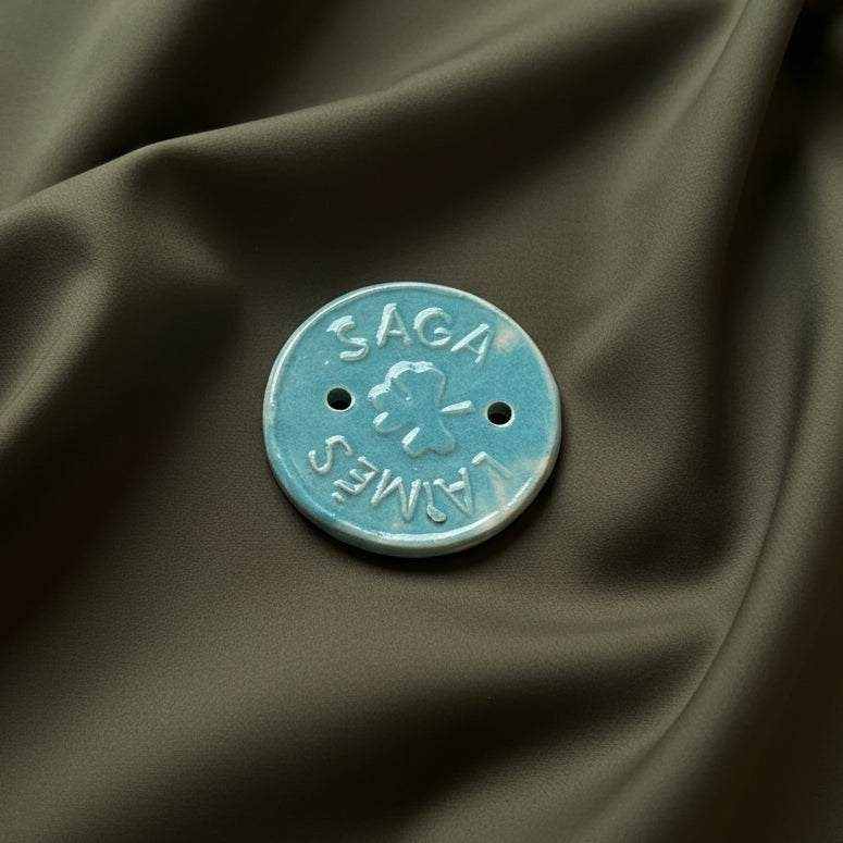 Keraminė Laimės saga su keturlapio dobilo simboliu ir mėlyna glazūra ant tamsios medžiagos fono