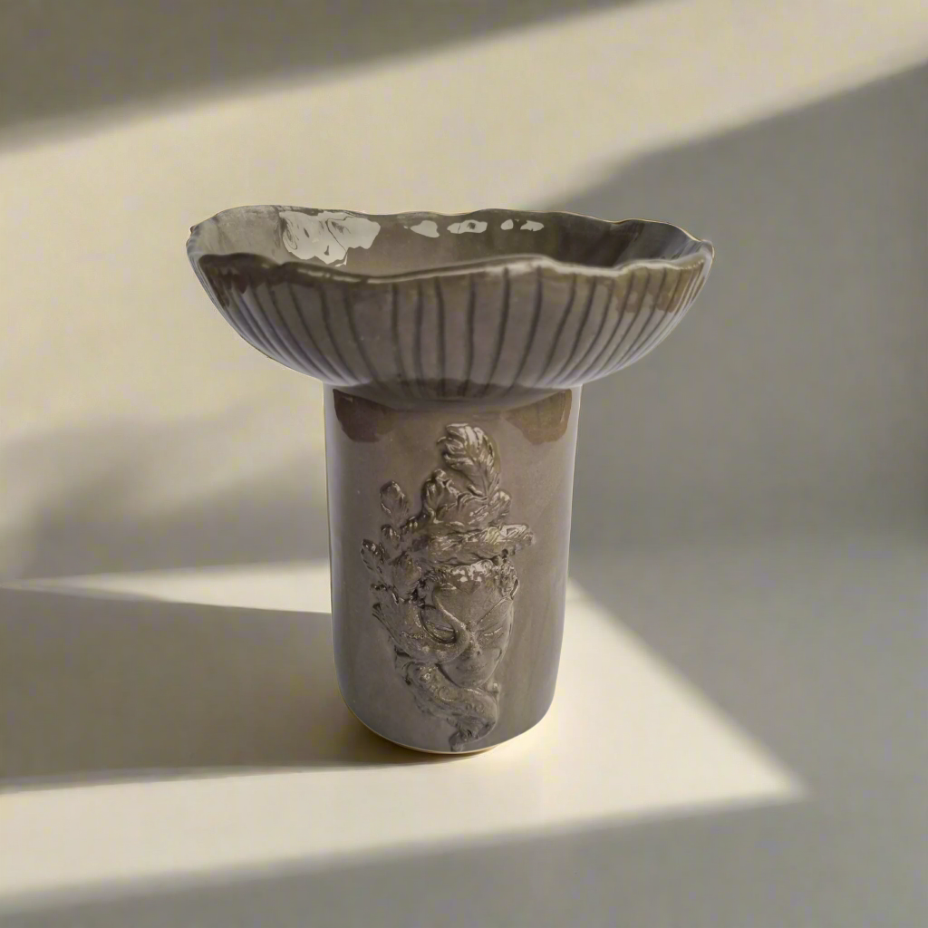 Pilkos spalvos molio vazelė "Madam paslaptis" su moters veido motyvu ir subtilia šypsena, dekoratyvi namų interjerui.